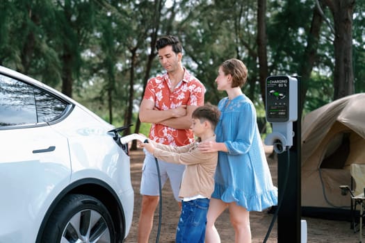 Outdoor adventure and family vacation camping in nature travel by eco friendly car for sustainable future. Lovely family recharge EV car with EV charging station in campsite. Perpetual