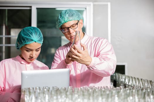 At a beverage factory line engineers meticulously check product bottles moving on the conveyor belt. Inspection and quality control managed by professionals with a laptop for assessments.