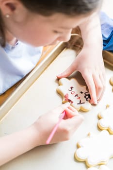 A heartwarming scene of a little girl carefully writing 'Sorry' on sugar cookies with food coloring, the cookies beautifully flooded with white royal icing.