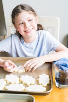 A heartwarming scene of a little girl carefully writing 'Sorry' on sugar cookies with food coloring, the cookies beautifully flooded with white royal icing.