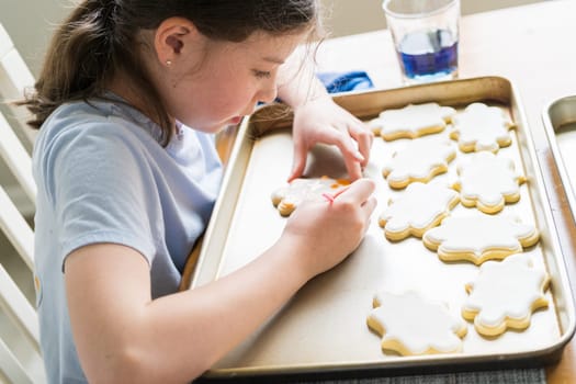 A heartwarming scene of a little girl carefully writing 'Sorry' on sugar cookies with food coloring, the cookies beautifully flooded with white royal icing.