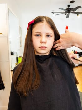 Gentle hands maneuver a hair dryer through a young girl's newly cut hair, showcasing the drying process after a meticulous trim. The warmth of the dryer breathes life into her locks, as they transform from damp to styled with care and expertise.