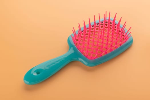 A vibrant teal and pink hairbrush isolated on a warm orange background, emphasizing simplicity and hygiene.