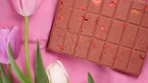 A bar of pink ruby chocolate with sublimated freeze-dried strawberries and almonds and spring tulip flowers . A dessert based on berries and nuts for International Women's Day, March 8, mother's day