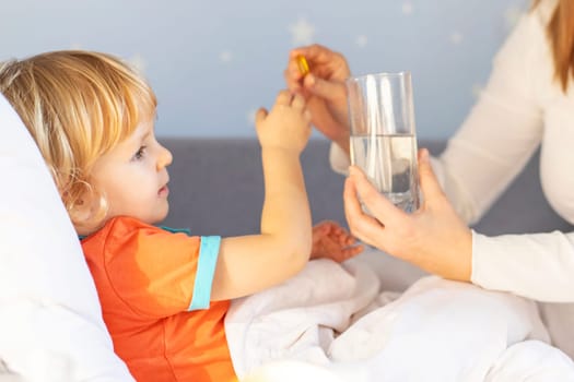 A tender moment as a mother in bed gives medicine to her attentive toddler, alongside a glass of water.