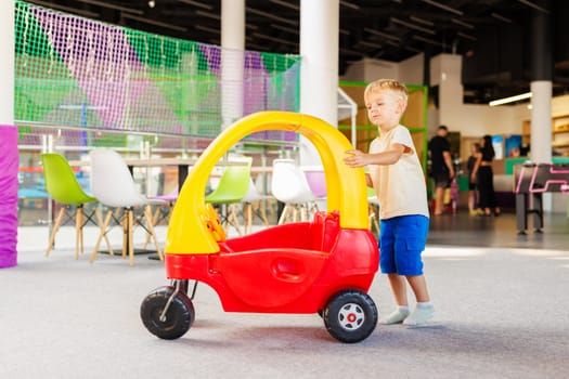 A young child enjoys playtime, pushing a colorful toy car in a vibrant indoor play area.