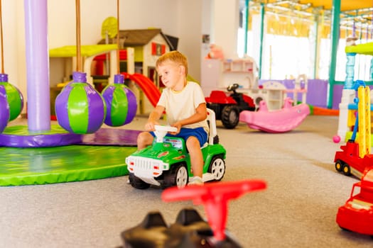 A child enjoys playtime, driving a toy car in a colorful indoor play area