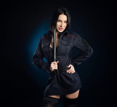 the sexy girl in a military police uniform on a dark background with handcuffs and a rubber baton