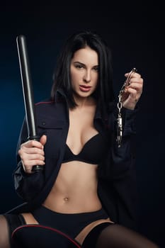 the sexy girl in a military police uniform on a dark background with handcuffs and a rubber baton