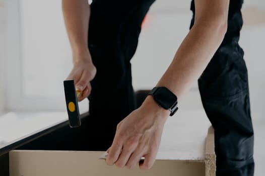 One young unrecognizable Caucasian man repairs the broken back wall of an old wardrobe with a hammer, close-up side view.