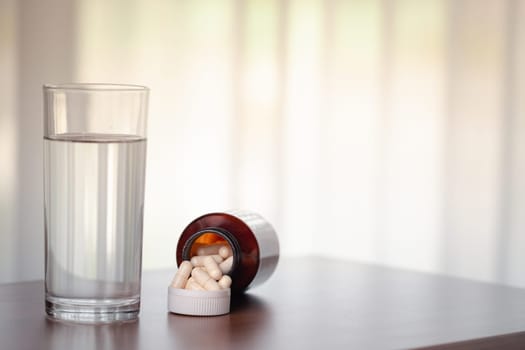 Pills and glass of water on wooden table in the room for medical and healthcare concept