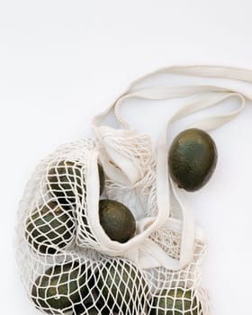 Avocados spilling from an eco-friendly net bag on a white background, concept of sustainable shopping