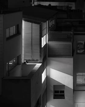 A black and white nocturnal urban scene featuring the architectural interplay of light and shadows