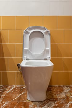 A pristine white toilet with open lid and seat set against a vibrant yellow and white tiled background