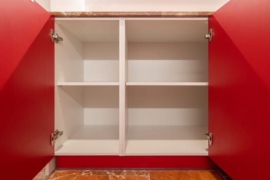 A vibrant red cupboard with its doors open revealing empty shelves, contrasting with a rustic terracotta floor