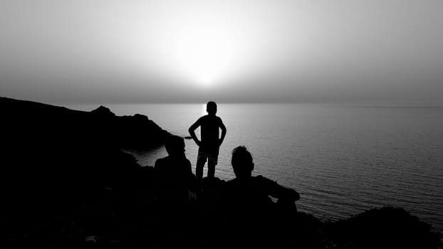 the silhouette of three people on the high coast during a sunset in black and white.