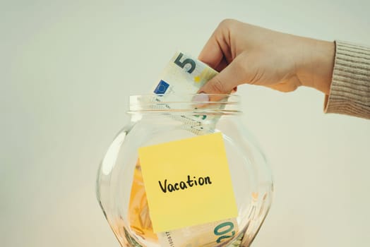 Person putting 5 euro banknote to the glass jar with inscription Vacation