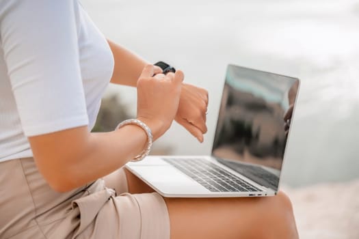 Freelance women sea working on the computer. Good looking middle aged woman typing on a laptop keyboard outdoors with a beautiful sea view. The concept of remote work