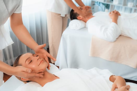 Caucasian couple enjoying relaxing anti-stress head massage and pampering facial beauty skin recreation leisure in dayspa modern light ambient at luxury resort or hotel spa salon. Quiescent