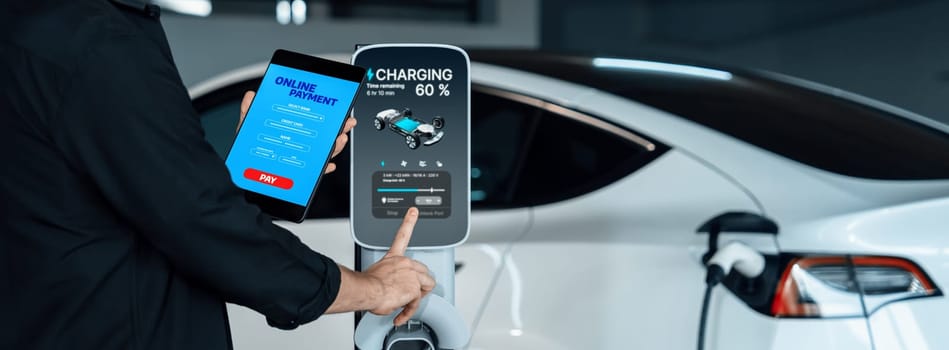 Young man travel with EV electric car to shopping center parking lot charging in downtown city showing urban sustainability lifestyle by green clean rechargeable energy of electric vehicle innards