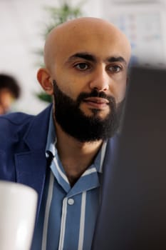 Business owner analyzing data on laptop while drinking coffee in office. Arab start up company executive manager planning strategy on portable computer on coworking space