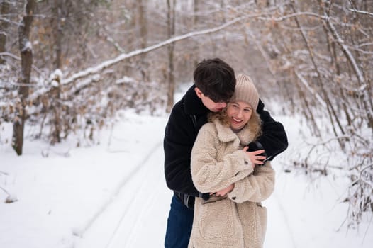 A young couple walks in the park in winter. Guy and girl hugging outdoors