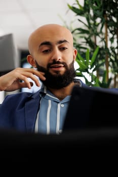 Arabian businessman having video call with coworker about startup project using digital tablet in coworking space. Executive discussing product launch with client in online meeting