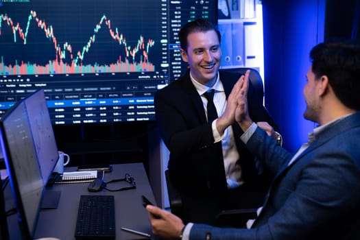 Two stock exchange traders getting profit in trading currency stock. Successful stock exchange showing financial benefit data on monitor screen at highest point of neon light at workplace. Sellable.