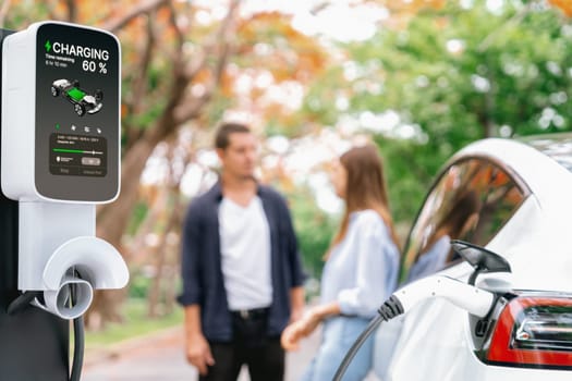 Lovely young couple recharging battery for electric car during autumnal road trip travel EV car in autumnal forest. Eco friendly travel on vacation during autumn. Exalt