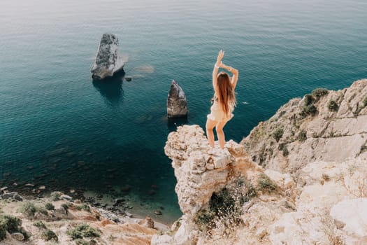 Woman travel sea. Happy tourist taking picture outdoors for memories. Woman traveler looks at the edge of the cliff on the sea bay of mountains, sharing travel adventure journey.