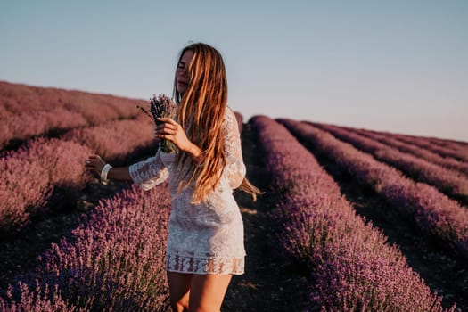 Close up portrait of young beautiful woman in a white dress and a hat is walking in the lavender field and smelling lavender bouquet.