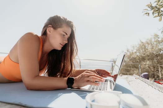 Digital nomad, Business woman working on laptop by the sea. Pretty lady typing on computer by the sea at sunset, makes a business transaction online from a distance. Freelance, remote work on vacation