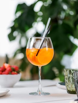 Typical summer drink Aperol Spritz aperitif served in wine glass with aperol, prosecco, soda, slice of orange. Glass of refreshing drink Aperol Spritz cocktail in restaurant with monstera background