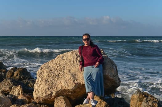 woman in a red jacket against the background of stones and the sea in winter in Cyprus 6