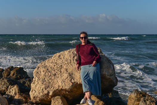 woman in a red jacket against the background of stones and the sea in winter in Cyprus 5