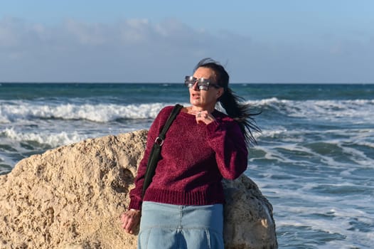 woman in a red jacket against the background of stones and the sea in winter in Cyprus 4