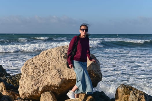 woman in a red jacket against the background of stones and the sea in winter in Cyprus 3