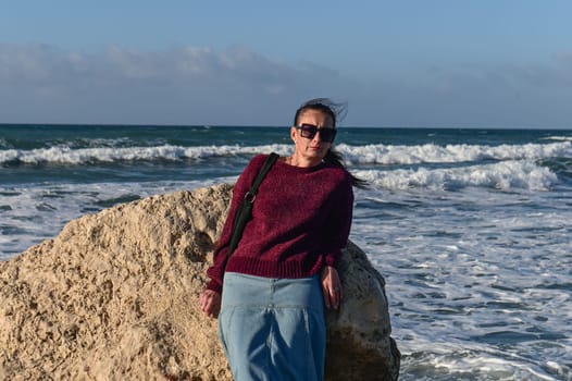 woman in a red jacket against the background of stones and the sea in winter in Cyprus 2