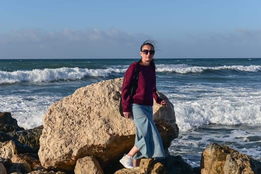 woman in a red jacket against the background of stones and the sea in winter in Cyprus 1