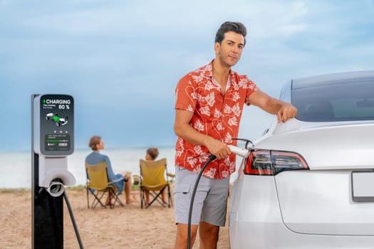 Family vacation trip traveling by the beach with electric car, dad or father recharge EV car while his family enjoy seascape beach. Family trip with alternative energy and eco-friendly car. Perpetual