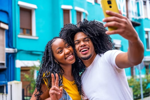 African couple gesturing success taking a selfie in a colorful street