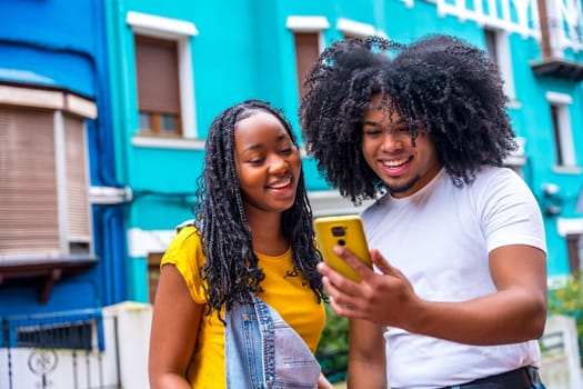 Young african friends using phone in the street next to colorful house