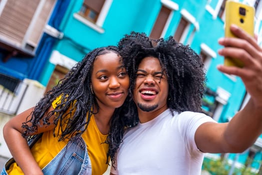 Smiling african couple pulling faces while taking selfie int he city in a colorful street