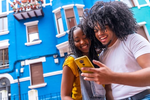 Low angle view portrait with copy space of a young african friends using phone standing in the street with blue colorful houses