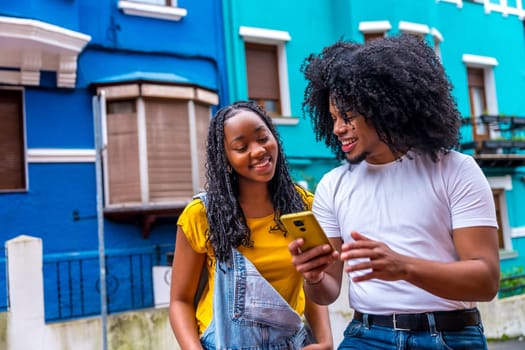 Afro cool friends using phone in the street next to blue colorful houses