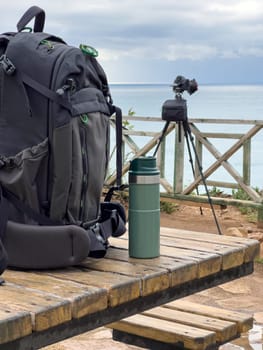 Photo backpack and thermos lie on the table in front of the camera