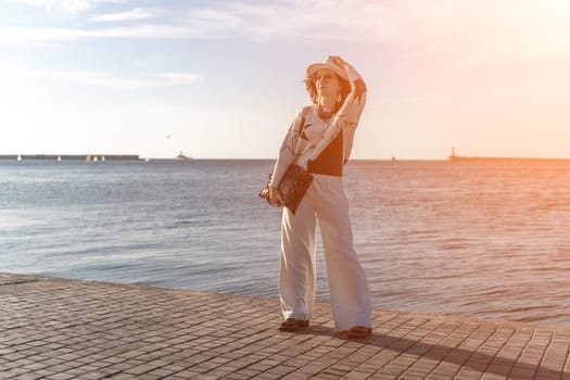 Stylish seashore woman. Fashionable woman in a white hat, white trousers and a light sweater with a black pattern on the background of the sea