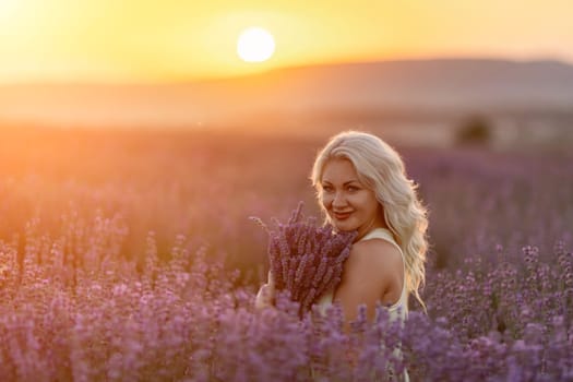 Blonde woman poses in lavender field at sunset. Happy woman in white dress holds lavender bouquet. Aromatherapy concept, lavender oil, photo session in lavender.