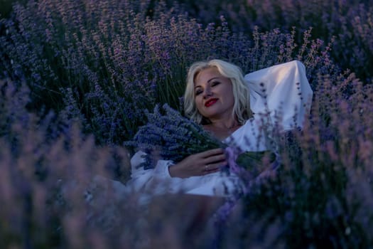 Blonde woman poses in lavender field at sunset. Happy woman in white dress holds lavender bouquet. Aromatherapy concept, lavender oil, photo session in lavender.