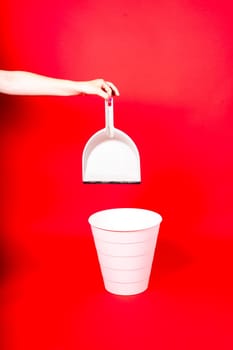 Woman throwing crumpled a paper from scoop into rubbish bin on red background